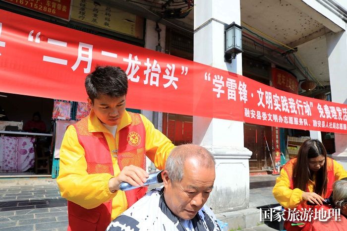 图2：3月11日，在广西柳州市融安县长安镇建设北街，志愿者为市民免费“剃龙头”。（谭凯兴 摄）